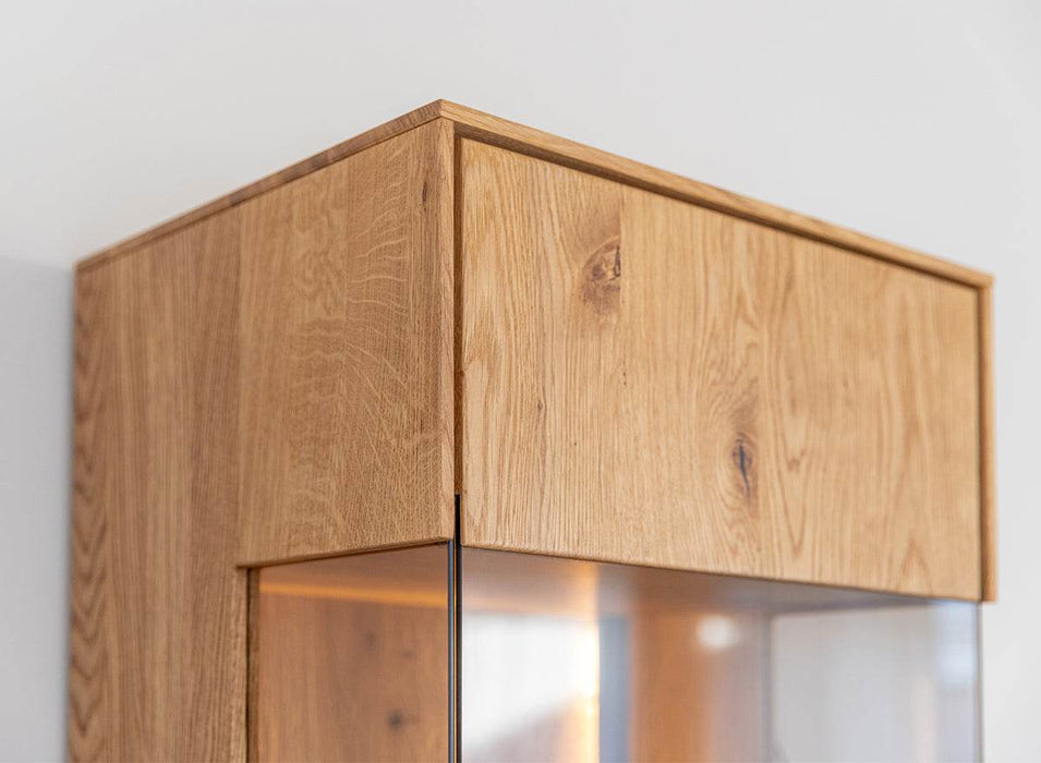 Beleuchtete Standvitrine Collodi aus massiver Eiche mit Rückwand in grober Holzstruktur -