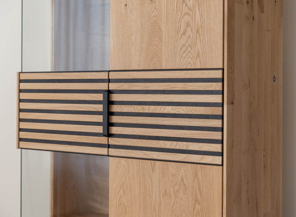 Beleuchtete Standvitrine aus massiver Eiche mit Lamellen | Wohnzimmerschrank Tirano II mit Rückwand in grober Holzstruktur -