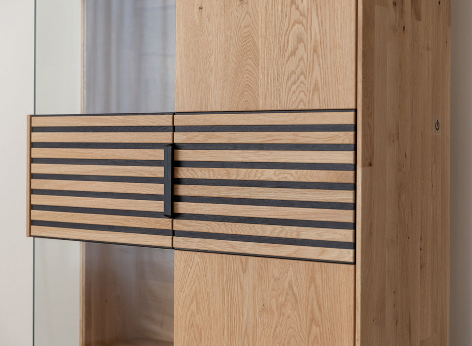 Beleuchtete Standvitrine aus massiver Eiche mit Lamellen | Wohnzimmerschrank Tirano II mit Rückwand in grober Holzstruktur